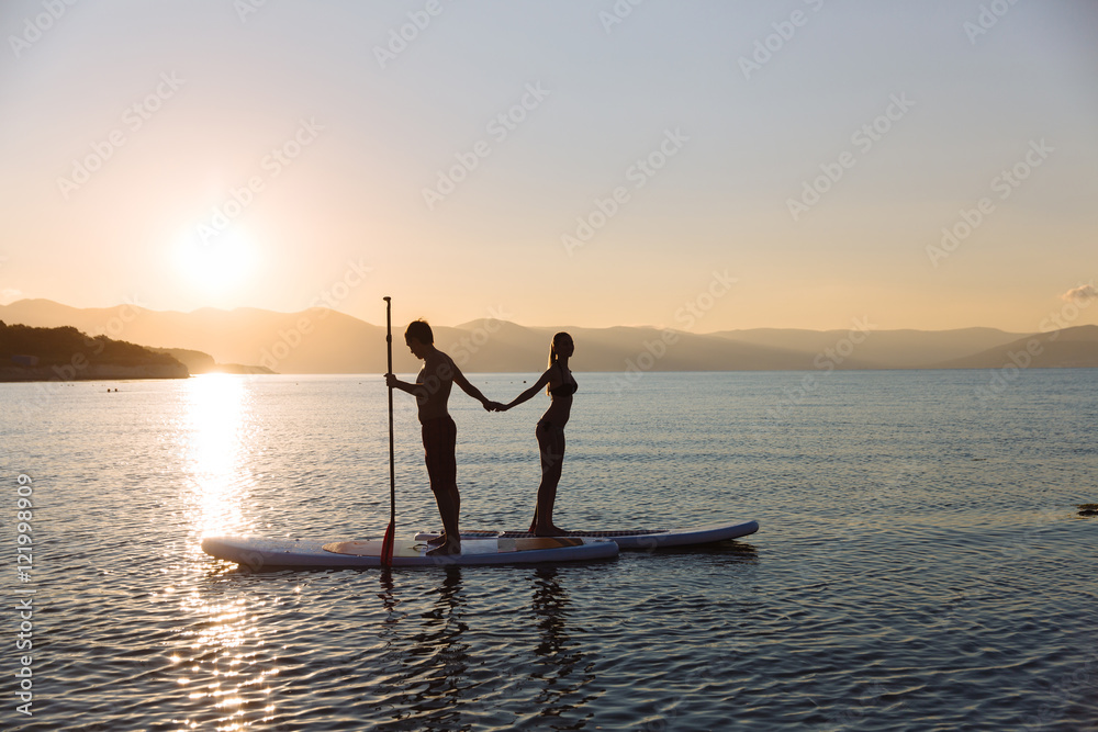 Silhouette of boy and girl on sup surf pull hands together at the ocean. Concept lifestyle, sport, love
