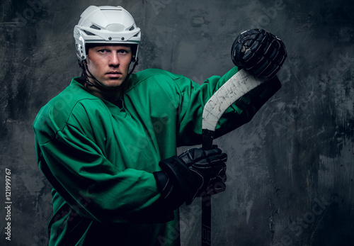 Hockey player in protective clothes holds playing stick.