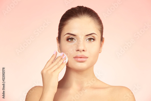 Beautiful young woman with face wipe on color background