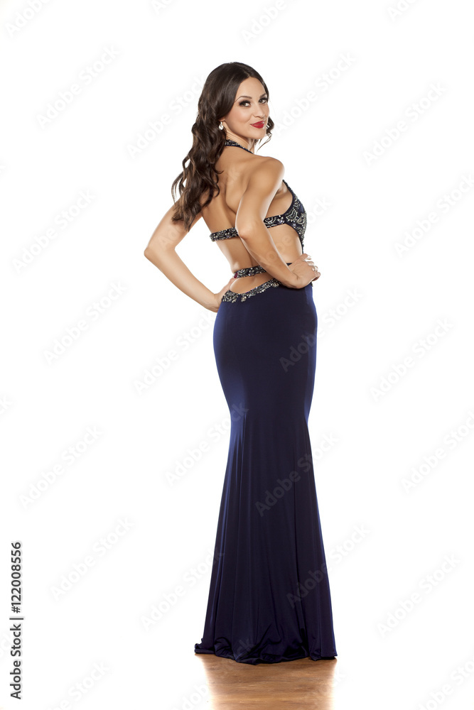 back view of a young woman posing in a long blue dress on a white background