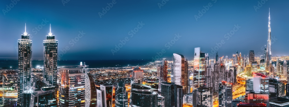 Naklejka premium Sceniczny widok z lotu ptaka w centrum Dubaj, Zjednoczone Emiraty Arabskie, z iluminującymi drapaczami chmur. Artystyczna panoramiczna linia horyzontu.