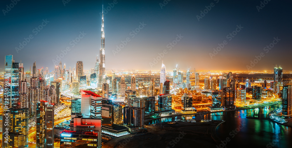 Fototapeta premium Aerial panorama view of a big futuristic city by night. Business bay, Dubai, United Arab Emirates. Colorful nighttime skyline.