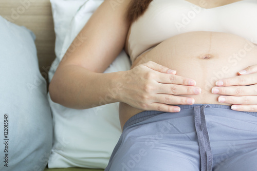 Pregnant woman hands holding belly on bed.