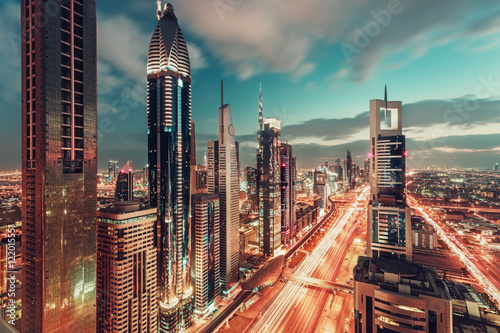 Bright colorful urban landscape of a big modern city with illuminated skyscrapers. Aerial view over downtown Dubai, UAE, with the famous highway. Artistic travel and architectural background.