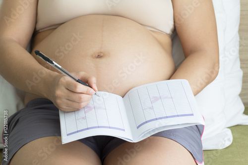 Pregnant woman record in note book in bedroom.