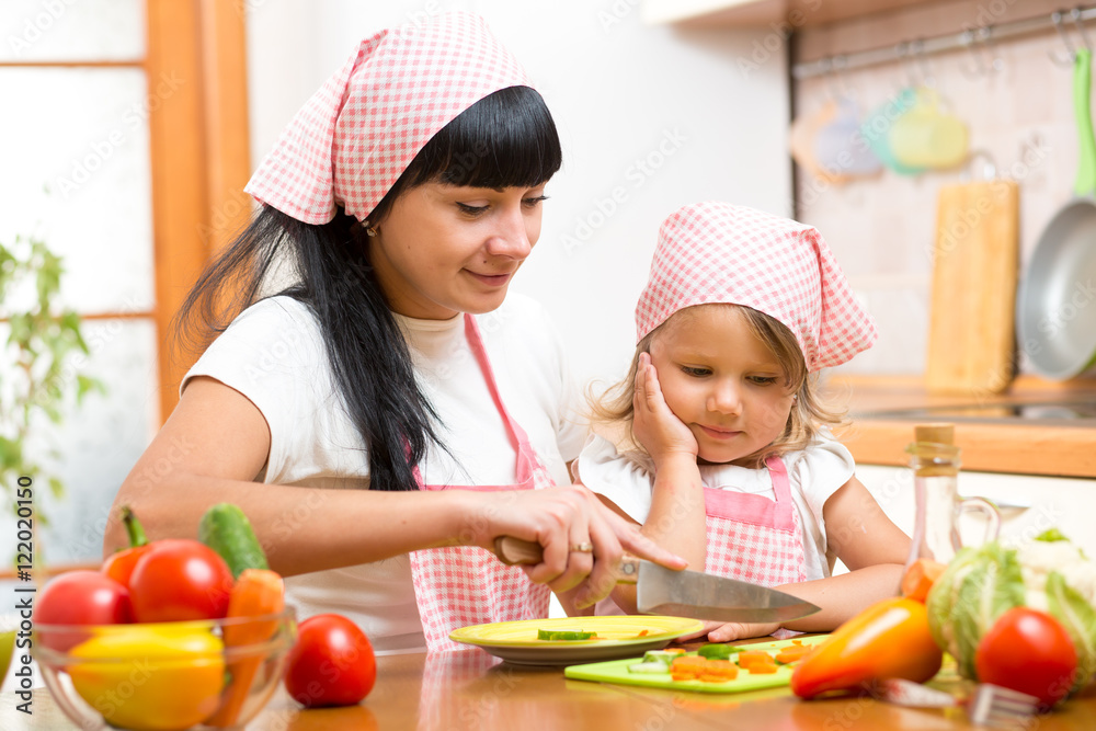 Mother teaching child making salad in kitchen. Mom and kid chopping vegetable on cutting board with knife. Cooking concept of happy family preparing food for dinner. Mother teaching child making salad in kitchen. Mom and kid chopping vegetable on cutting board with knife. Cooking concept of happy family preparing food for dinner.