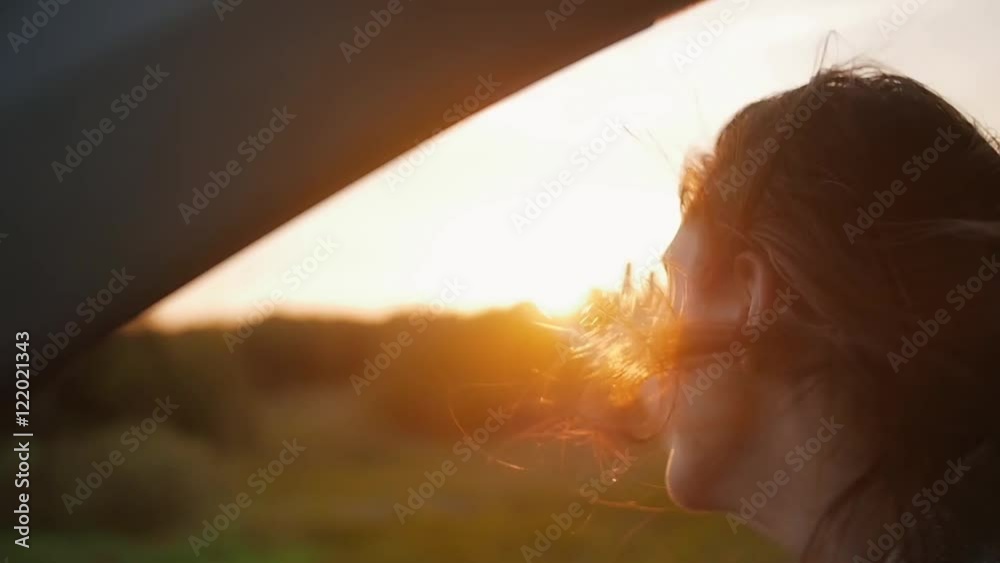 Sunset in the nature. Woman in a car, hand playing in the air. Sunset rays through the trees. Wind blows hair. Slow mo