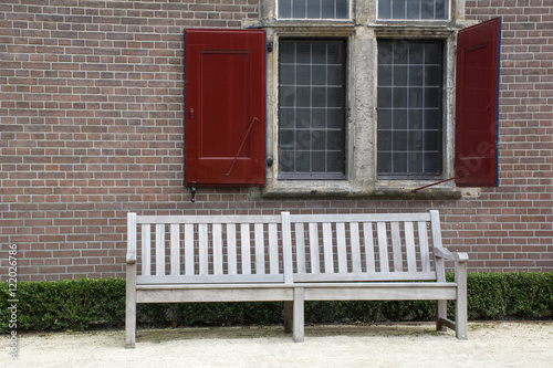 Street wooden bench near the brick wall with window and red shutters