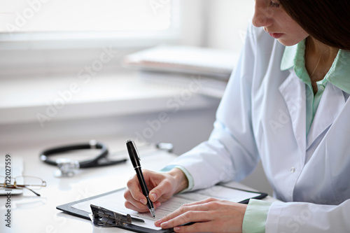 Close up of unknown female doctor sitting at the table near the window in hospital and typing at laptop computer