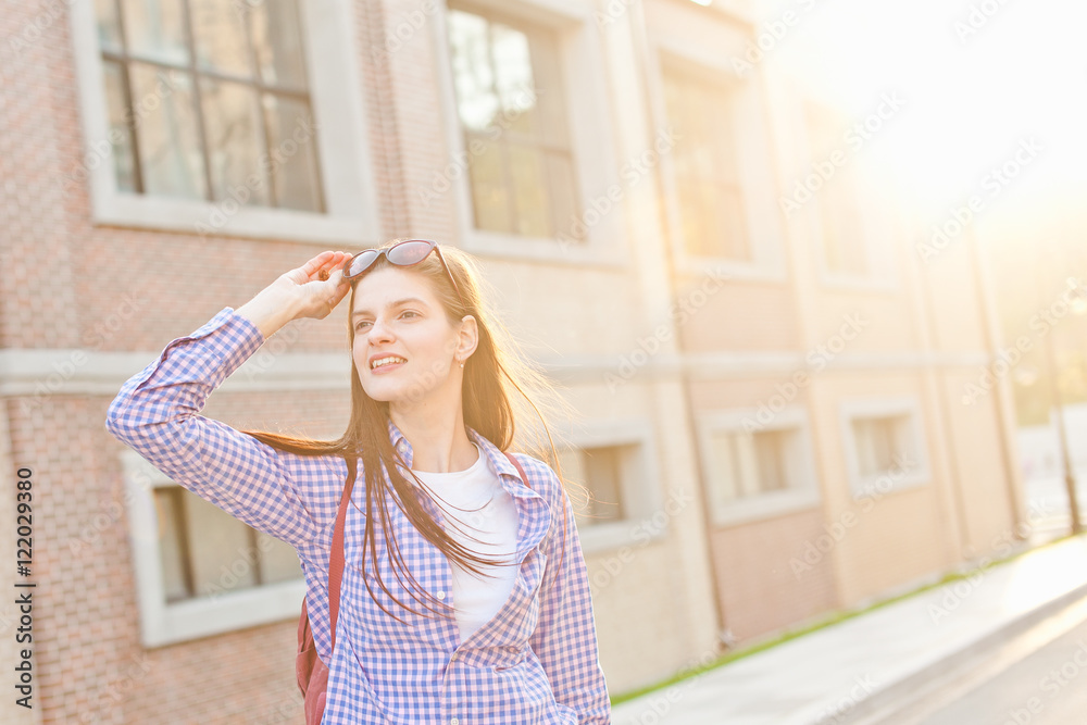 Young curious girl looks away holding sunglasses with sunset bac