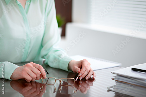 Business woman hands in a green blouse sitting at the desk in the office and holding glasses, the right window . She is thinking about the business problems, the successes, the concepts