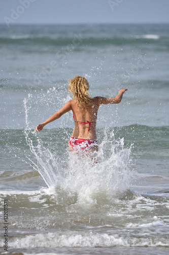 Back view of woman in bikini running into the water