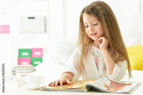 Beautiful little girl reading magazine 