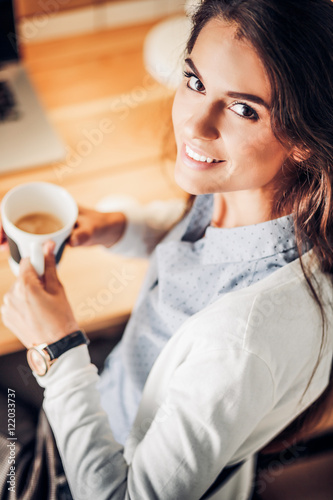 Portrait of relaxed young woman sitting at her desk holding cup of coffee