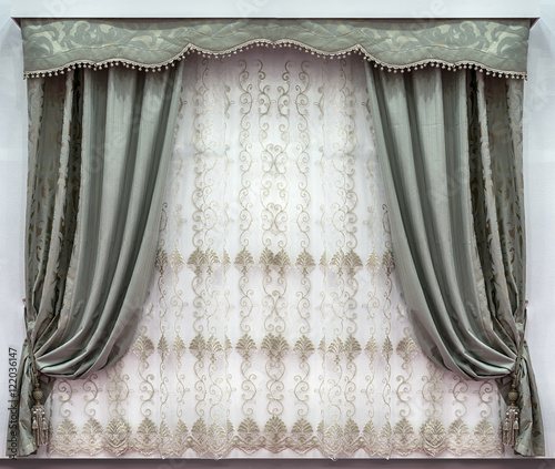 The stylish design of the windows in the interior. Combined curtains made of the natural fabrics. A hard pelmet and a tulle with embroidery