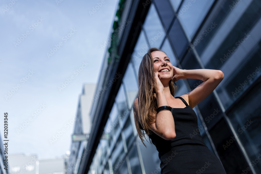 Happy Young Woman in Black Dress Talking on Cellphone in the City