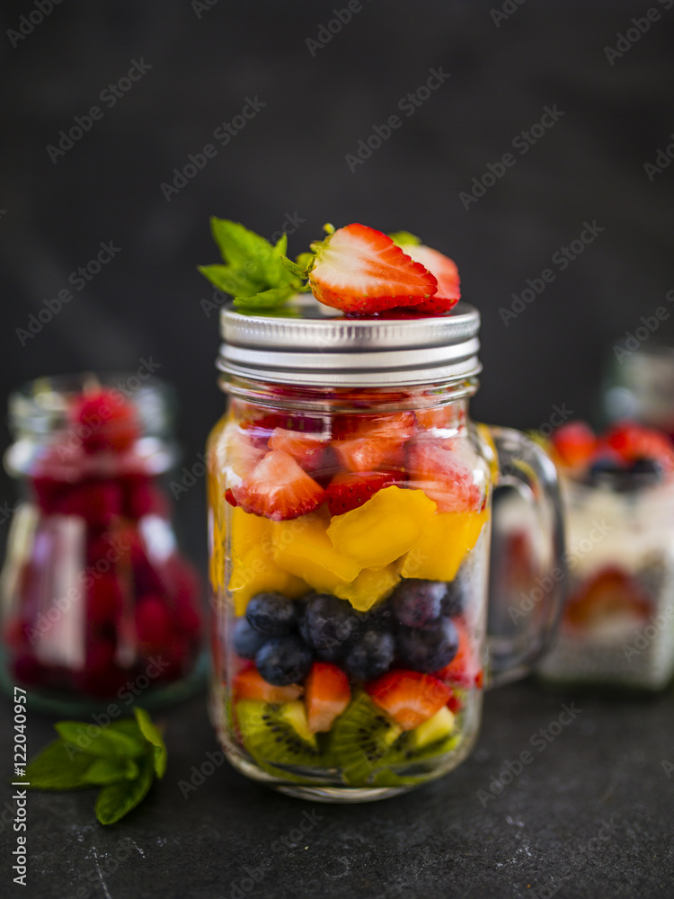 Fruit salad and fresh berries fruit in a glass jars on stone background. Fruit salad and fresh berries fruit in a glass jars on stone background.
