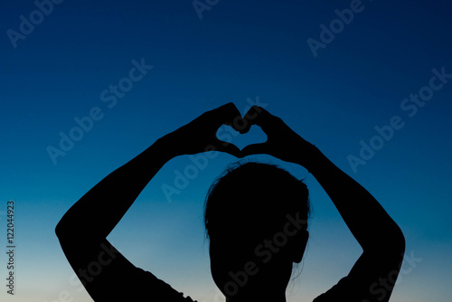 silhouette of woman Hand-made heart-shapedon on sky at sunset.