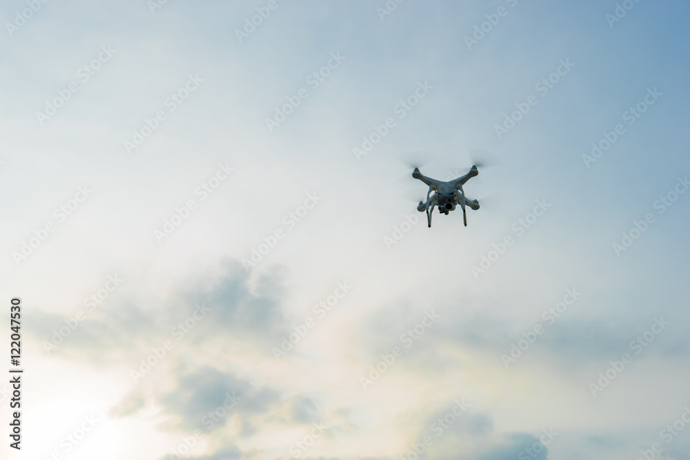 White drone hovering in a bright blue sky and clouds White drone hovering in a bright blue sky and clouds