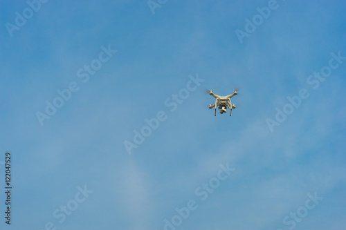 White drone hovering in a bright blue sky and clouds