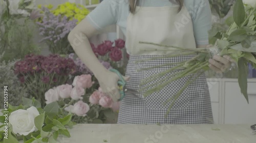 Florist woman trimming stems of a beautiful flower bouquet with scissors, ungraded tone photo