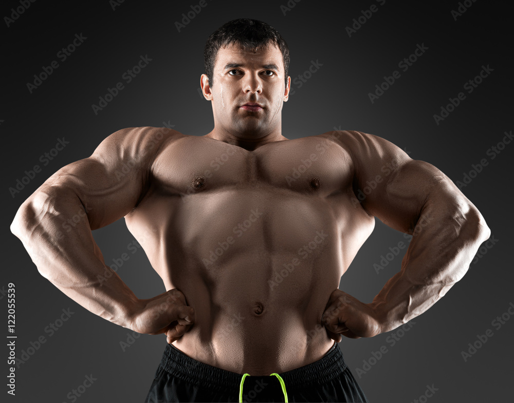 Handsome muscular bodybuilder posing over black background.