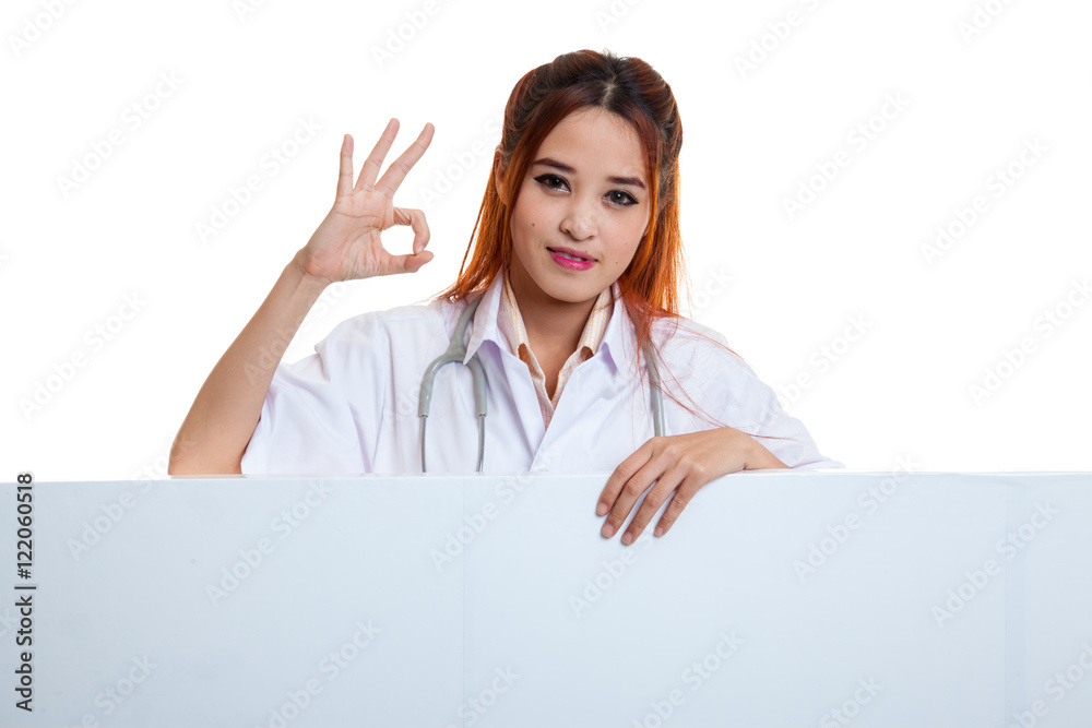 Young Asian female doctor show OK sign behind blank white billb Young Asian female doctor show OK sign behind blank white billb