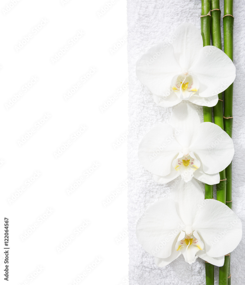 Fototapeta premium Three orchids and branches of bamboo lying on white towel. Viewed from above. Spa concept.