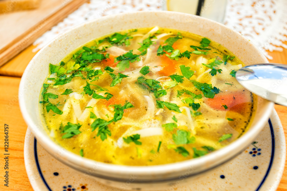 Chicken noodle soup in cream colored ceramic bowl with handles