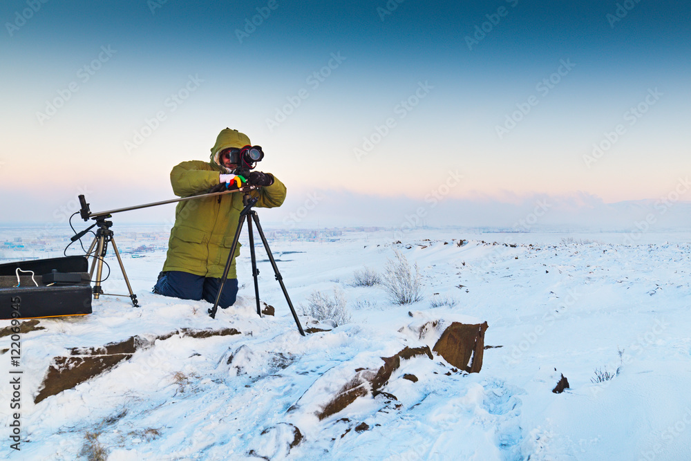 Man with photo camera on tripod taking timelapse photos in the arctic tundra.