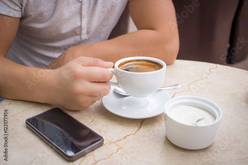 Male hand with cup of coffee, smartphone on table top