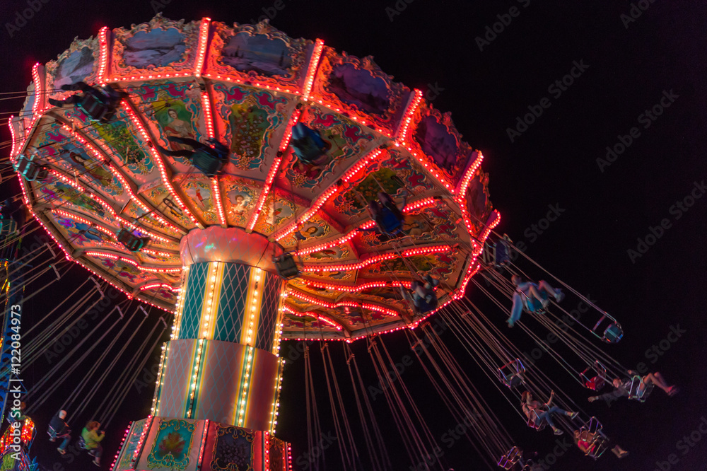 people spinning around fast and high in swings at the brightly lit ride ...