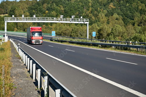 Obraz na płótnie Electronic toll collection with a passing red truck on a highway on the forest background. w salonie