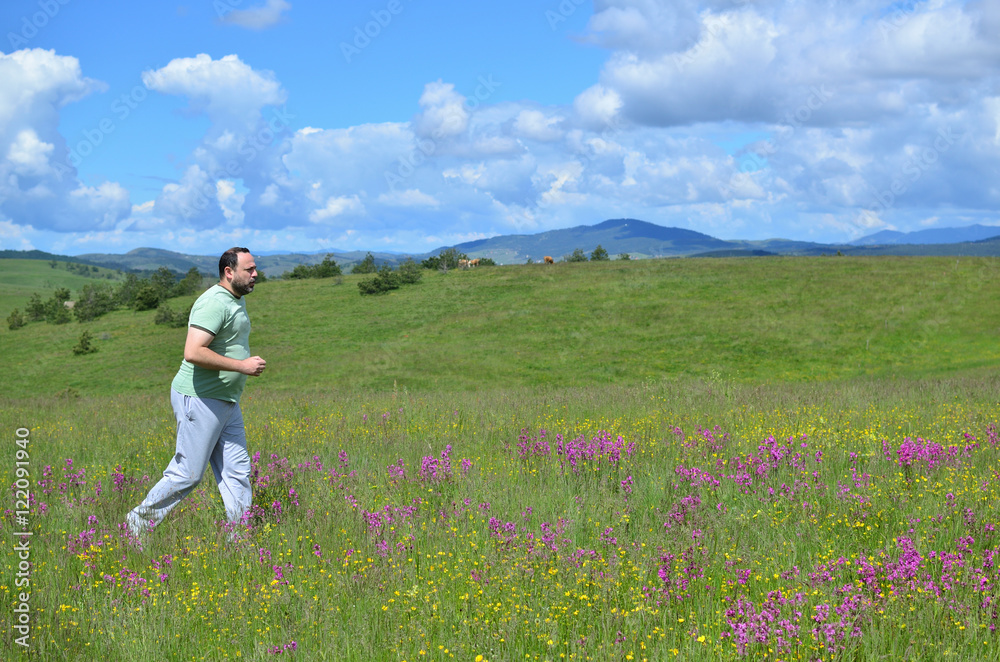 Man jogging in a meadow with wildflowers on cloudy day in springtime and with hills in background Man jogging in a meadow with wildflowers on cloudy day in springtime and with hills in background