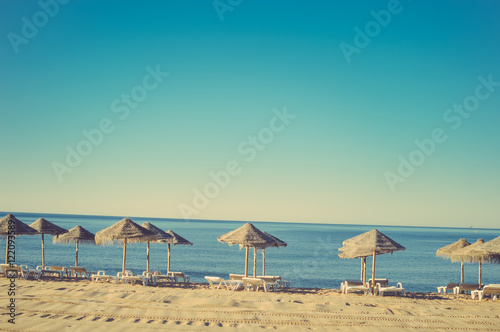 Fototapeta Naklejka Na Ścianę i Meble -  Beautiful view of beach with wicker umbrellas on the sunny blue sky outdoors background
