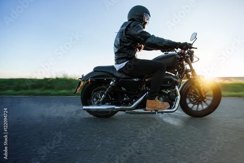 Man sat on motorcycle on the road during sunset. Chopper high power motorcycle goes over landscape.