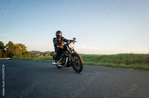 Man sat on motorcycle on the road during sunset. Chopper high power motorcycle goes over landscape.