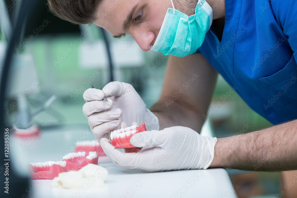 Dental prosthesis, dentures, prosthetics work. Prosthetics hands while working on the denture, false teeth, a study and a table with dental tools. Dental prosthesis, dentures, prosthetics work. Prosthetics hands while working on the denture, false teeth, a study and a table with dental tools.