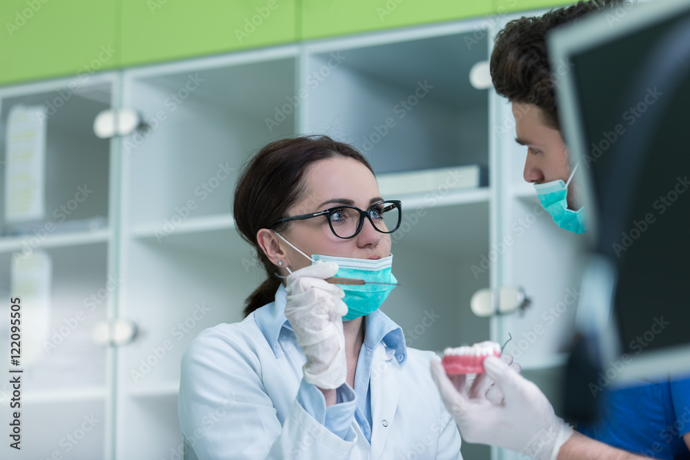Dental prosthesis, dentures, prosthetics work. Prosthetics hands while working on the denture, false teeth, a study and a table with dental tools. Dental prosthesis, dentures, prosthetics work. Prosthetics hands while working on the denture, false teeth, a study and a table with dental tools.