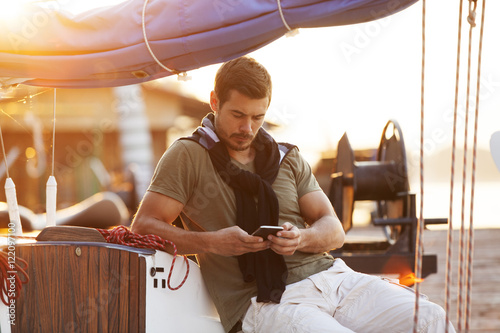 Handsome man using cellphone on sailing boat in sunset