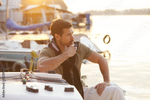 Handsome man on sailing boat in sunset.