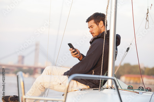 Handsome man using cellphone on sailing boat in sunset