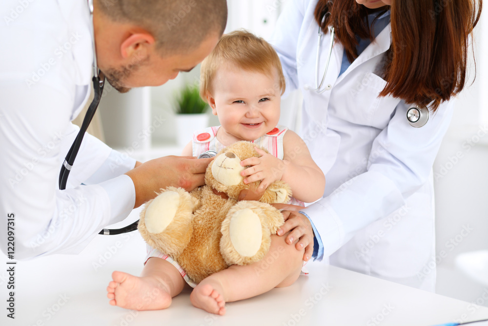 Two pediatricians are taking care of baby in hospital. Little girl is being examining by doctor with stethoscope. Health care, insurance and help concept. Two pediatricians are taking care of baby in hospital. Little girl is being examining by doctor with stethoscope. Health care, insurance and help concept.