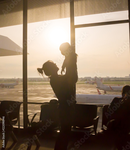 Silhouette of  Mother raising her little daughter up high at airport with airplane is background 