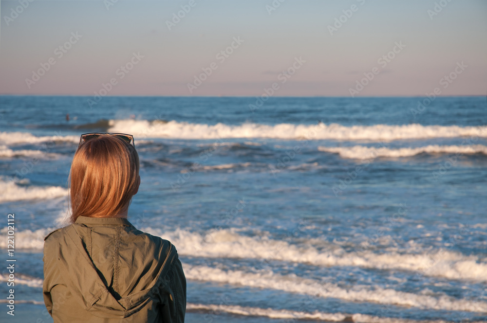 Beautiful young woman sitting on beach, looking at waves