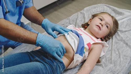 Little girl lying on examination bed and smiling as doctor pressing on her stomach