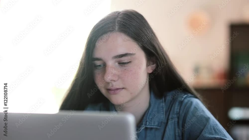 Close-up portrait of teenage girls using a laptop sitting at table at home