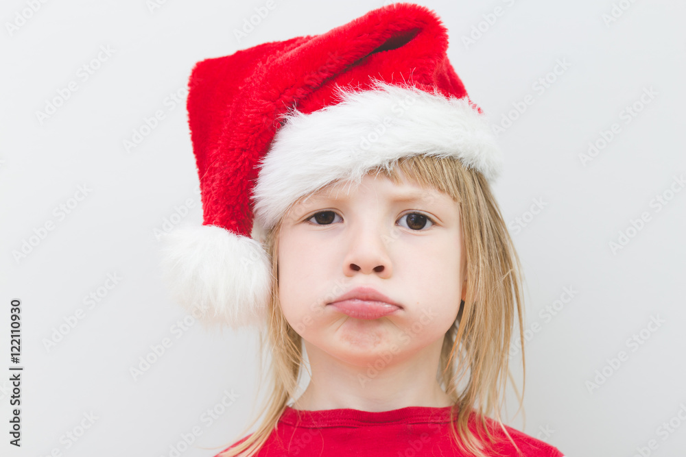 portrait of disappointed little blond girl wearing santa claus hat with big sad dark eyes, no jolly, no present