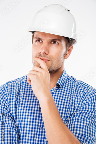 Pensive young man building engineer in helmet standing and thinking