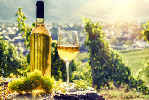 Bottle and full glass of white wine over vineyard background photo